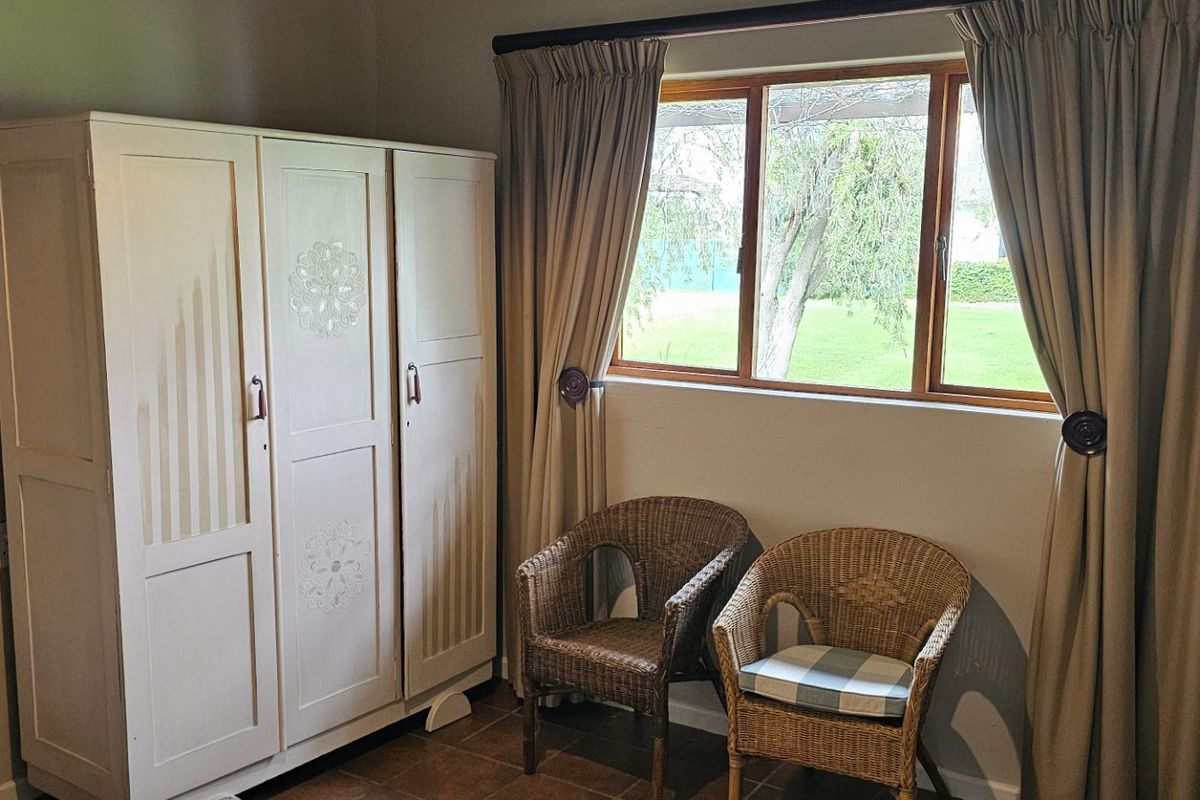 A bedroom featuring tiled flooring, a built-in wardrobe, and a timber-framed window with garden views.