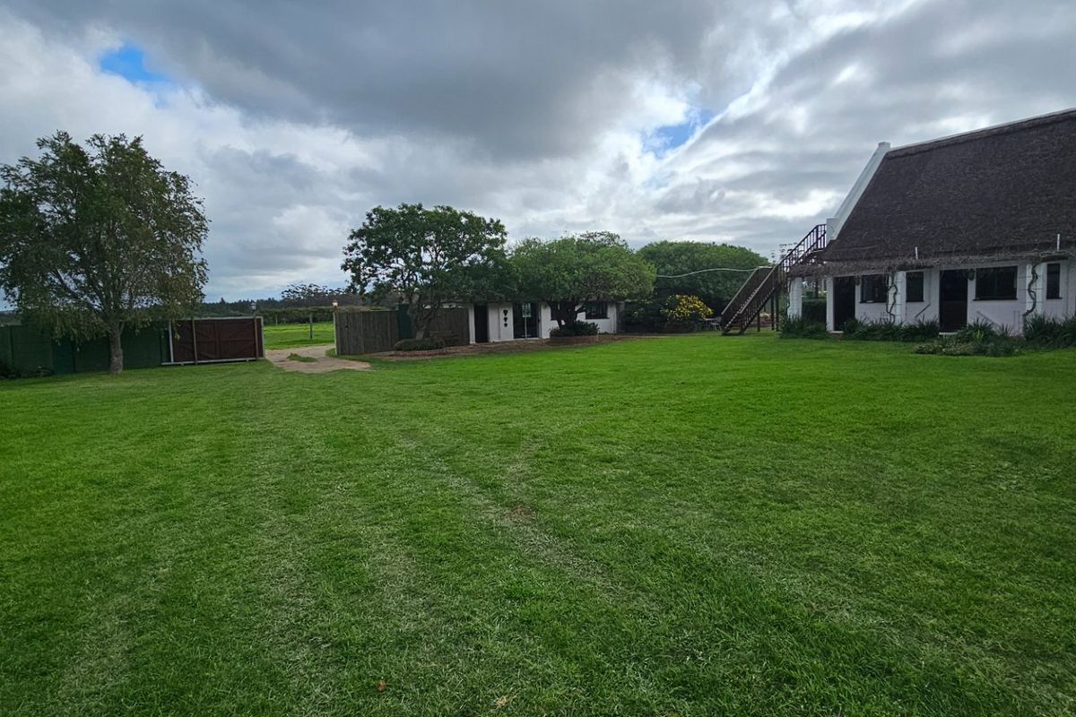 A spacious rear garden area featuring a large lawn and a building with a traditional thatched roof and external staircase access.