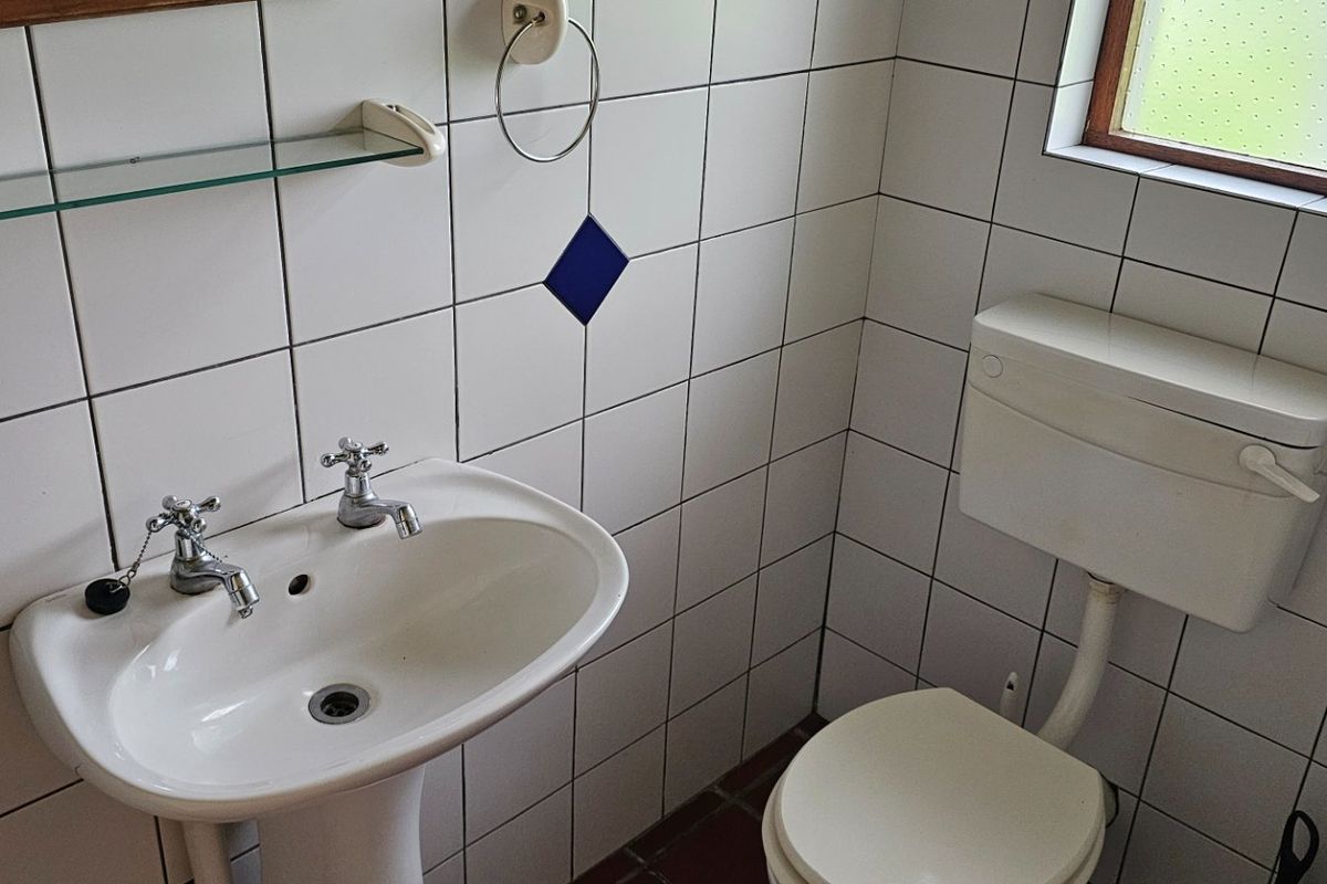A compact bathroom featuring a pedestal basin, toilet, and white ceramic wall tiles with decorative accents.