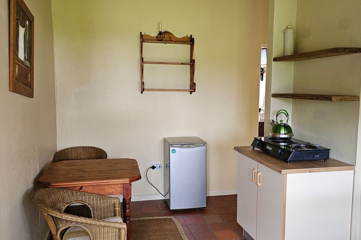A compact kitchen area featuring terracotta floor tiles, built-in base cabinetry, and wooden floating shelves, providing a functional and efficient space.