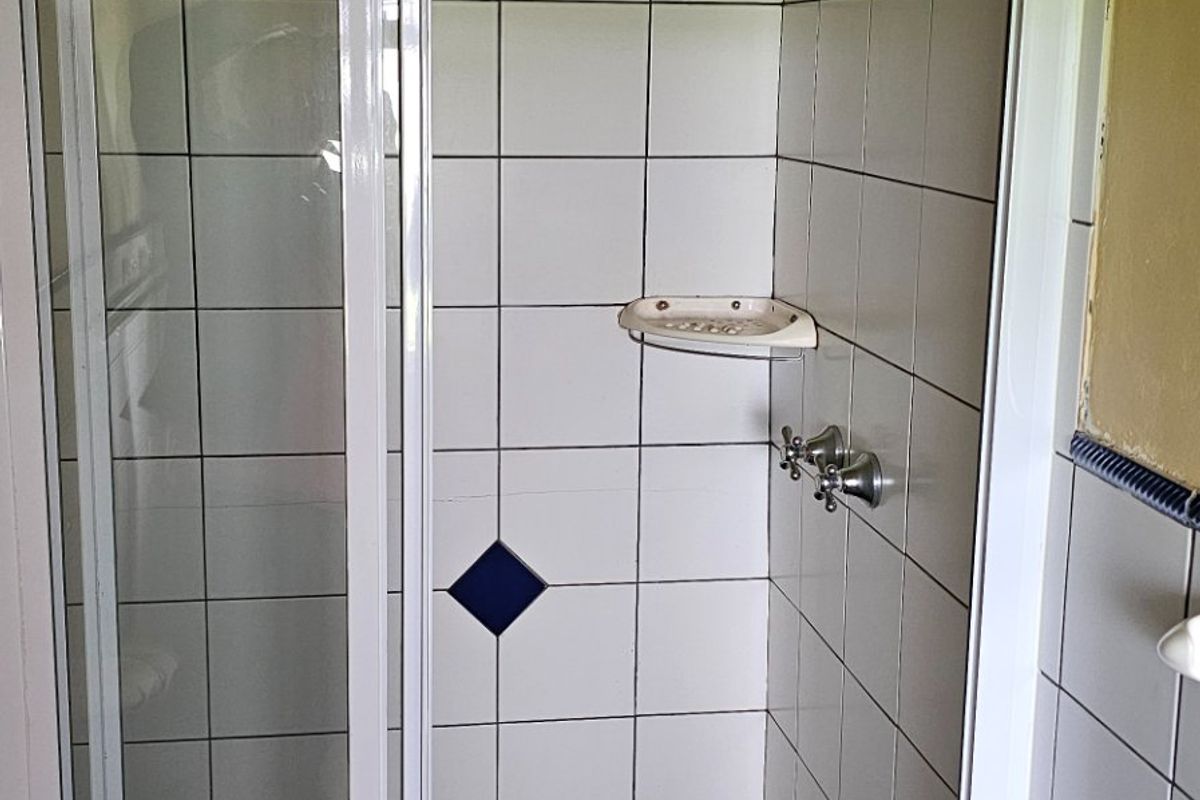 A functional shower stall featuring white wall tiles, a dark tiled floor, and a standard shower mixer with a built-in soap dish.