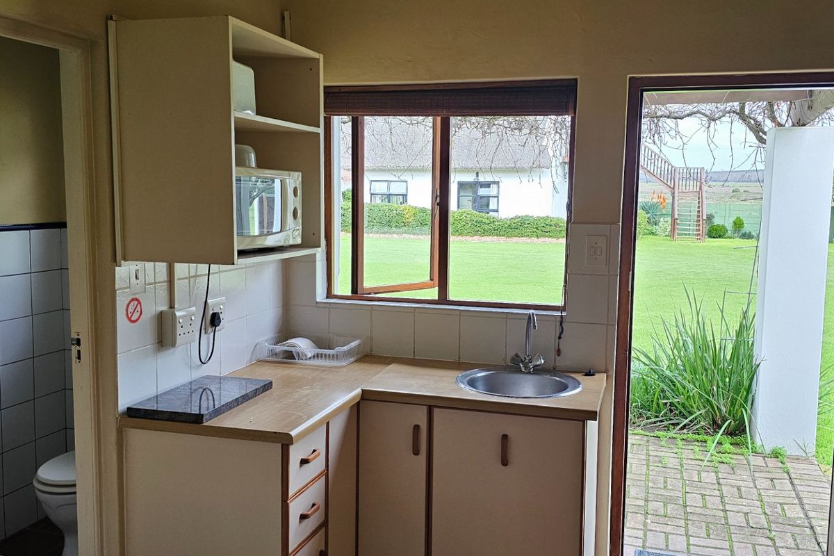 A compact scullery area featuring built-in cabinetry, a stainless steel sink, and direct access to an outdoor patio area.