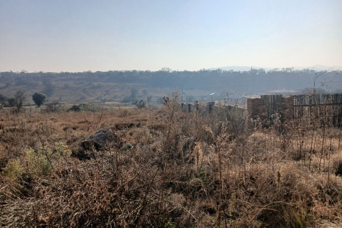 A view of the vacant residential land featuring natural vegetation and a boundary fence with a distant landscape backdrop.