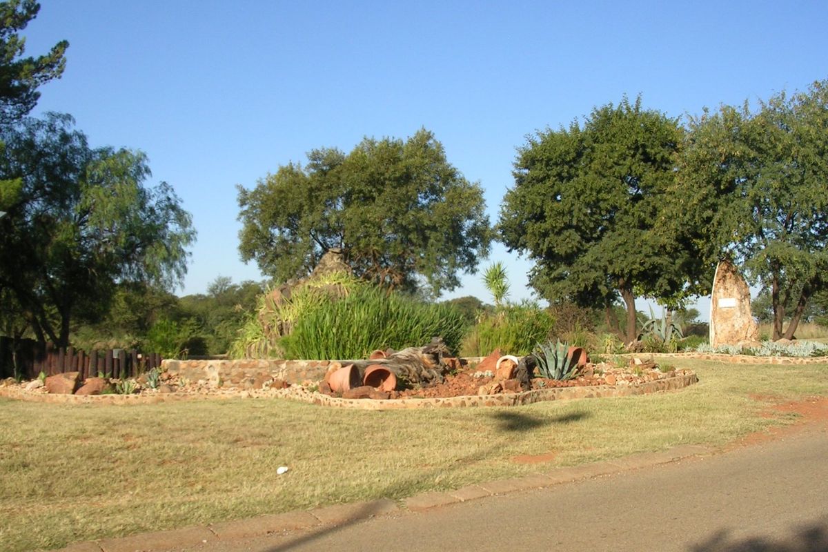 A landscaped garden area featuring mature trees, stone retaining walls, and established greenery adjacent to a paved driveway.