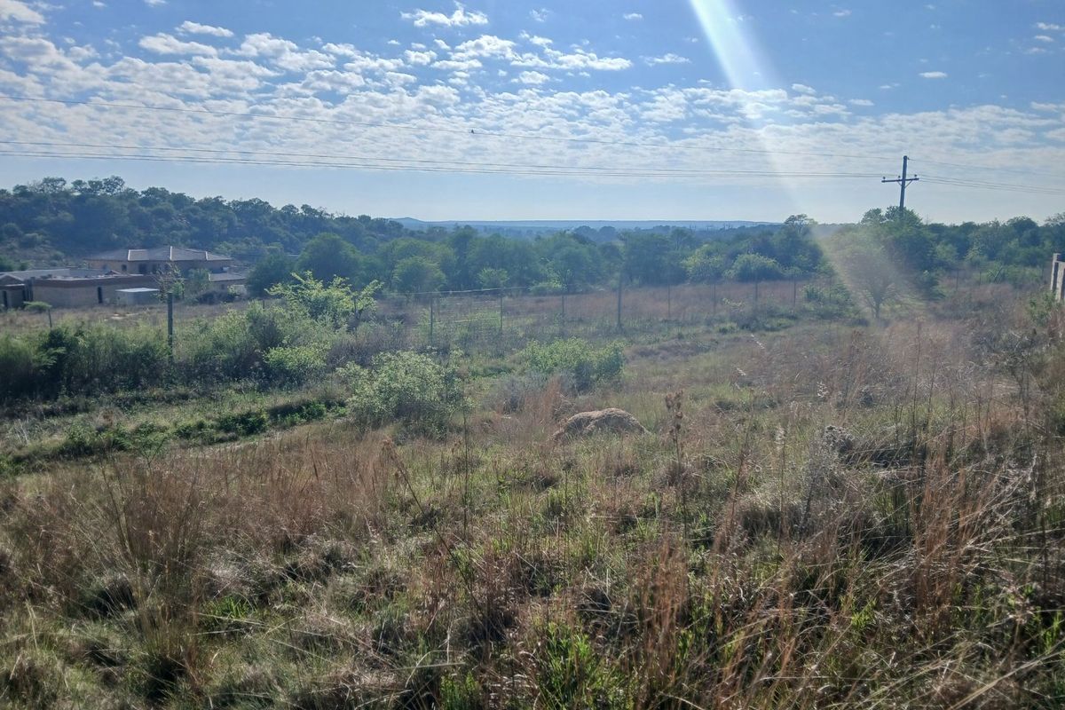 A wide-angle view of the vacant residential land, featuring natural vegetation, perimeter fencing, and distant landscape views under a clear sky.