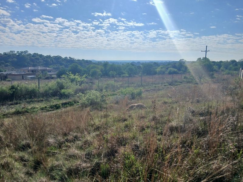 A wide-angle view of the vacant residential land, featuring natural vegetation, perimeter fencing, and distant landscape views under a clear sky.