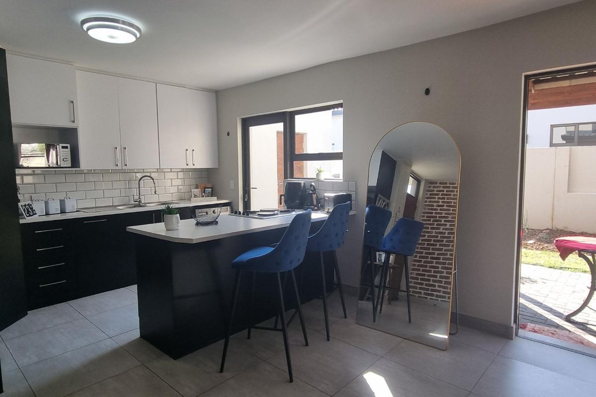 Modern kitchen featuring a central island, sleek black and white cabinetry, subway tile backsplash, and direct access to an outdoor patio area.