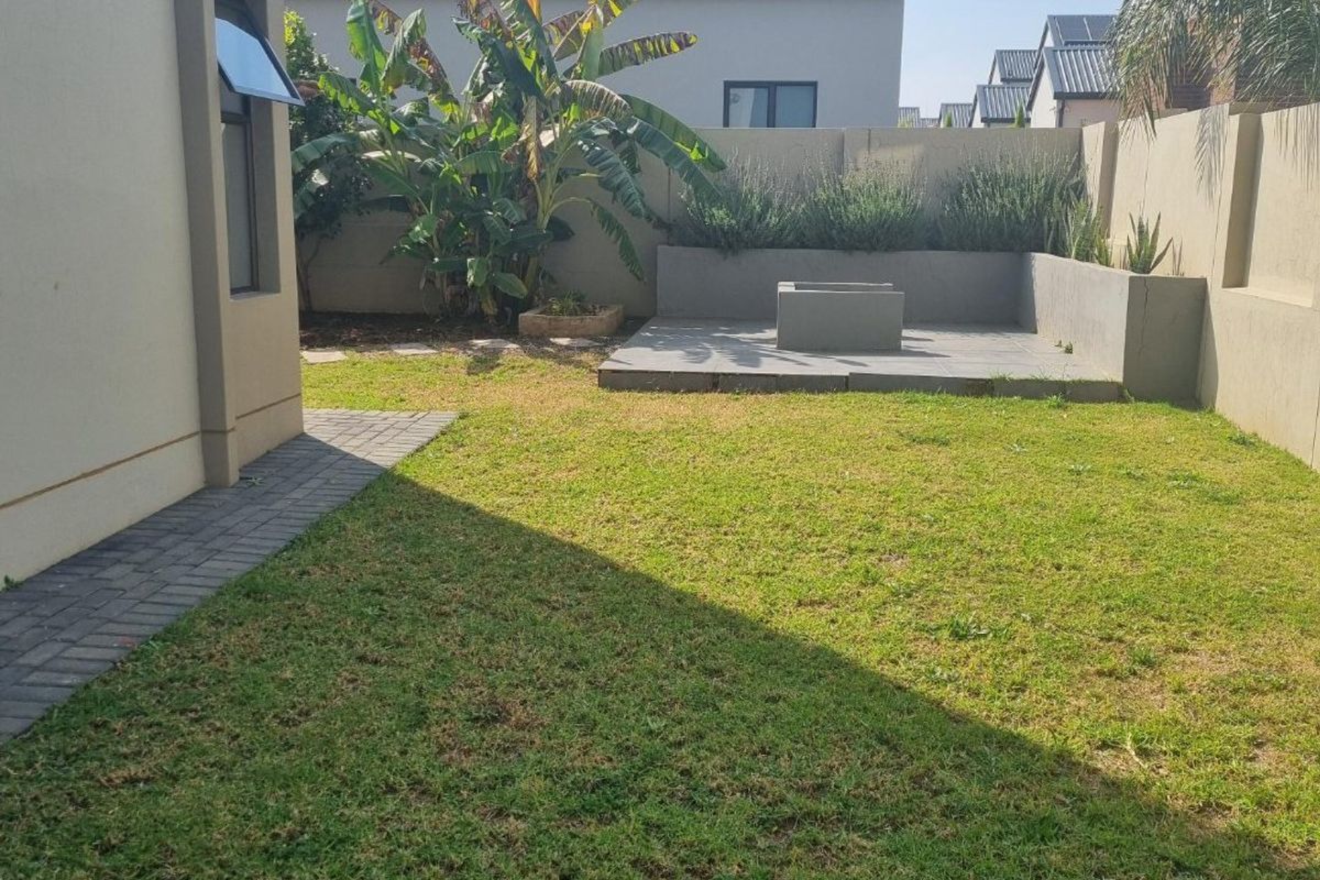 A private rear garden featuring a manicured lawn, paved walkway, and a built-in concrete fire pit area enclosed by boundary walls.