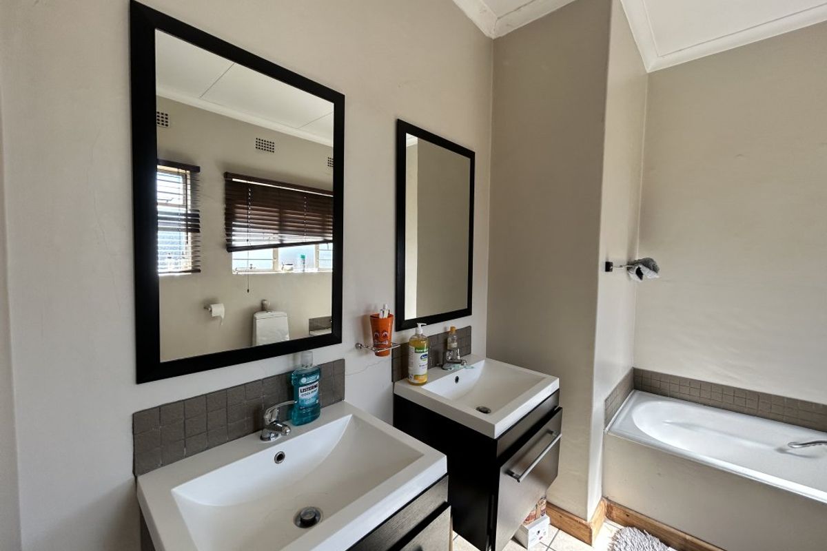 A functional bathroom featuring a double vanity with modern basins, wall-mounted mirrors, and a built-in bathtub with tiled surround.