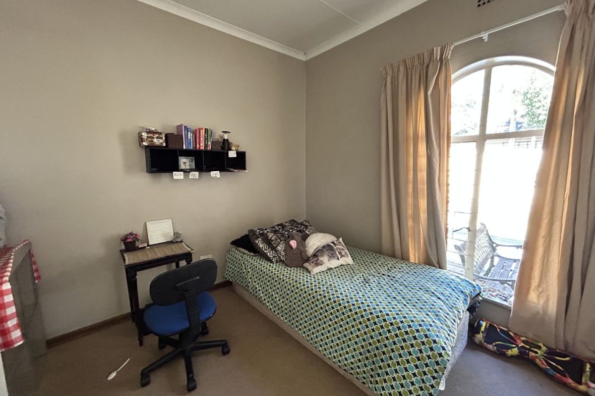 A functional bedroom featuring an arched window, neutral wall tones, and carpeted flooring, offering a comfortable and well-lit living space.