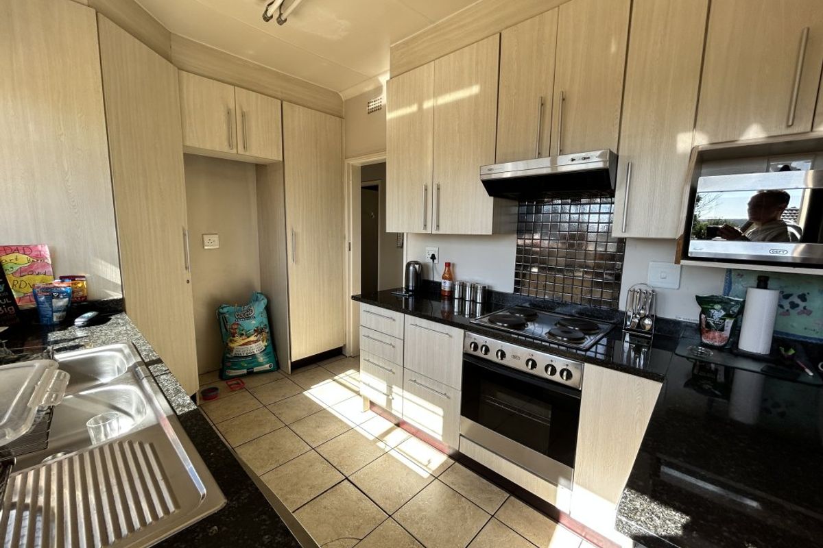 A functional kitchen featuring light wood-finish cabinetry, granite countertops, a built-in oven with hob, and a tiled backsplash.