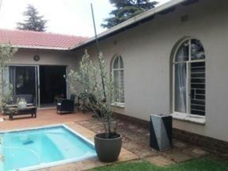A rear exterior view featuring a swimming pool, tiled patio area, and arched windows with security bars on the main house structure.