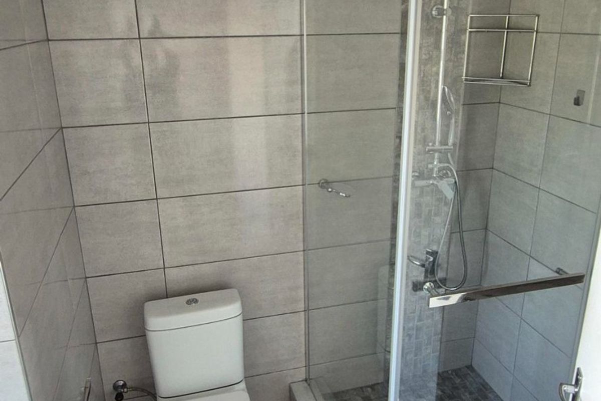 A clean, modern bathroom featuring a glass-enclosed shower, neutral wall and floor tiling, and a standard toilet.