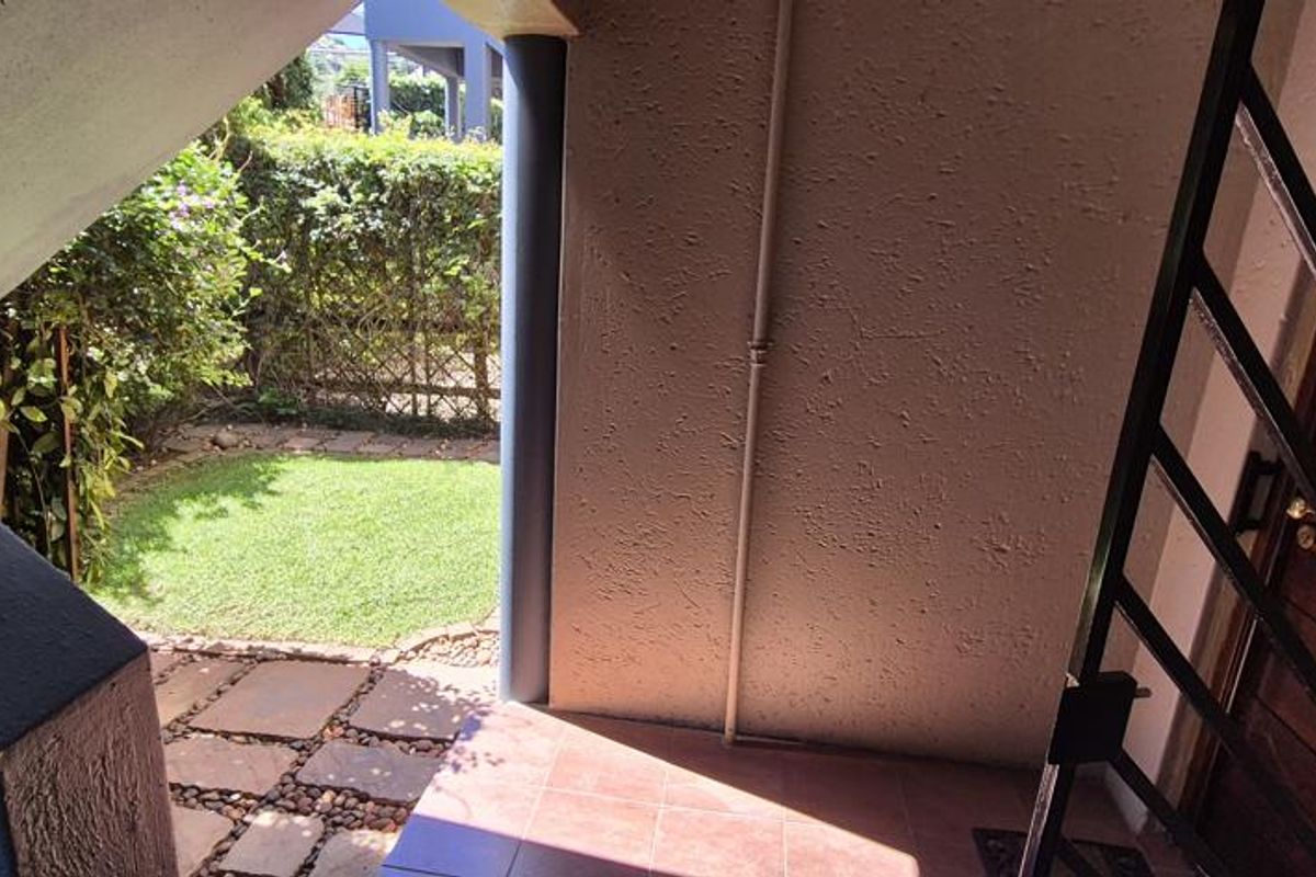 A covered entrance area featuring a security gate, timber door, and tiled flooring, providing access to the property with a view of the garden.
