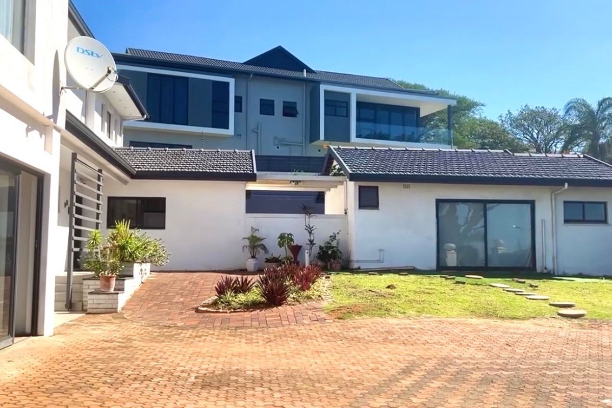 Rear view of a multi-level residential property featuring a paved courtyard, landscaped garden area, and modern sliding glass doors.