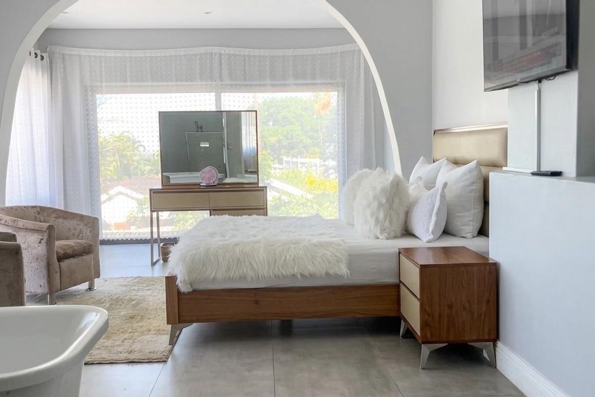Spacious bedroom featuring a large arched opening, tiled flooring, and a sliding glass door providing natural light and garden views.