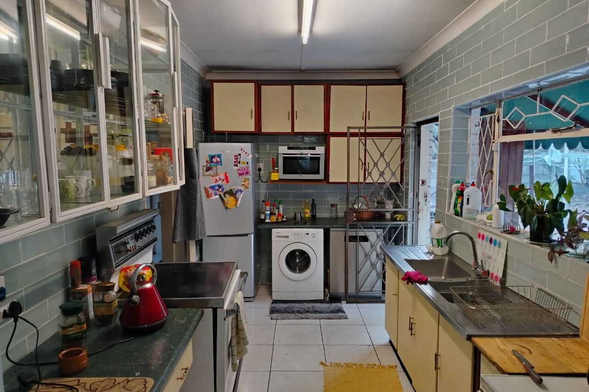 A functional kitchen featuring tiled walls, built-in cabinetry, a stainless steel sink, and integrated appliances, offering potential for a modern renovation.