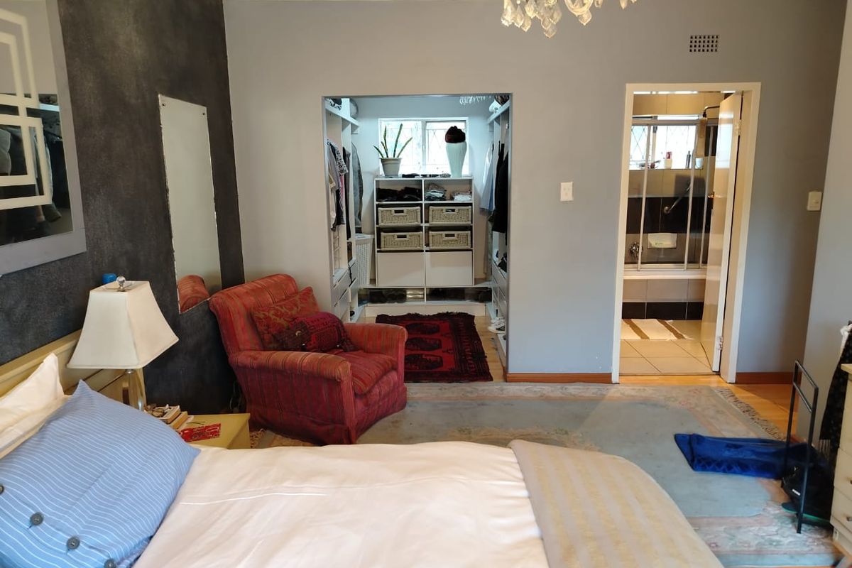 Spacious bedroom featuring an integrated walk-in closet and an en-suite bathroom, complemented by laminate flooring and decorative ceiling cornice.