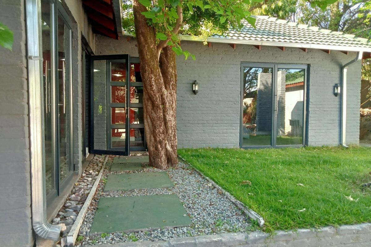 Rear exterior view featuring painted brick walls, modern aluminium sliding doors, and a landscaped garden area with a paved walkway.