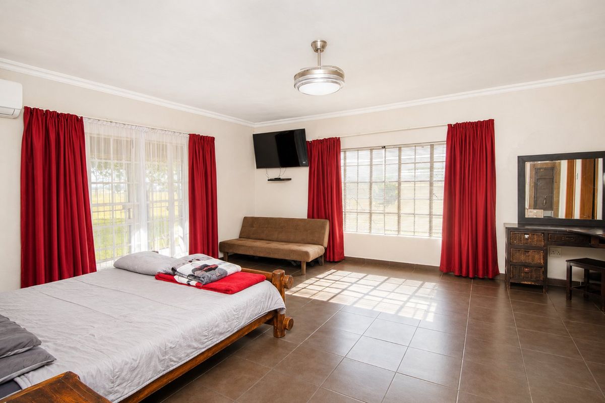 Spacious bedroom featuring tiled flooring, an integrated air conditioning unit, ceiling fan, and large windows providing ample natural light.