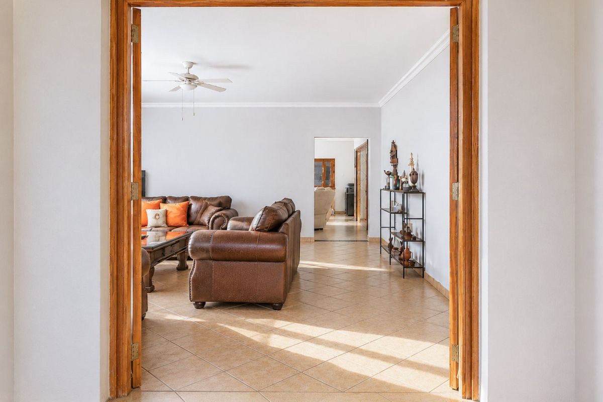 A spacious living area featuring tiled flooring, coved cornicing, and a ceiling fan, viewed through a classic wooden doorway.