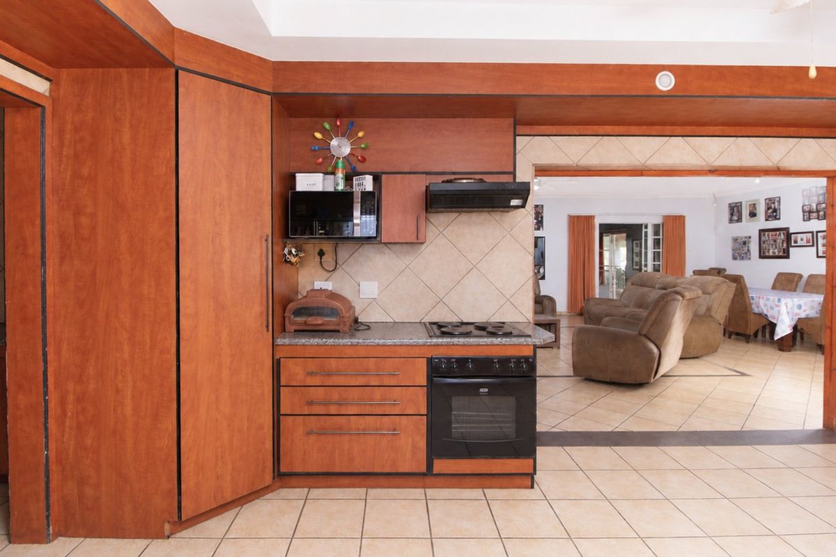 A functional kitchen featuring wood-finish cabinetry, built-in oven and hob, tiled backsplash, and flooring, with an open-plan flow into the adjacent living area.