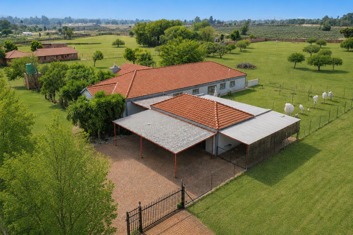 Aerial view of a farm property featuring a main residence with a terracotta roof, attached carport, paved driveway, and expansive surrounding grounds.