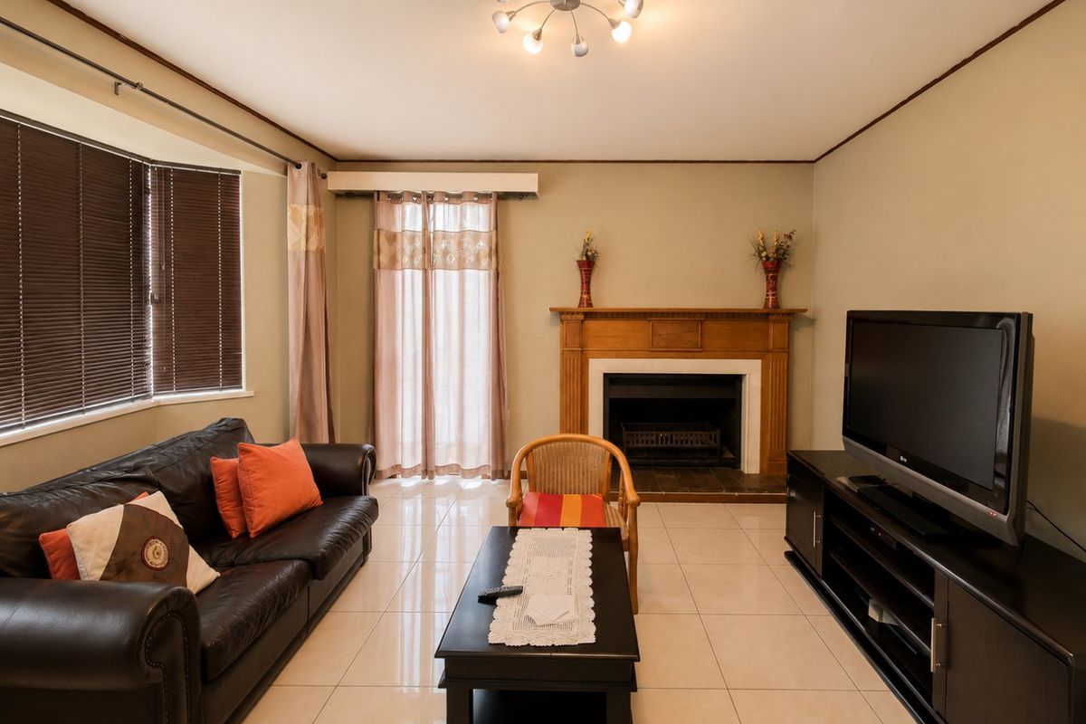 A living room featuring tiled flooring, a central fireplace with a wooden mantelpiece, and natural light from the window and sliding door.