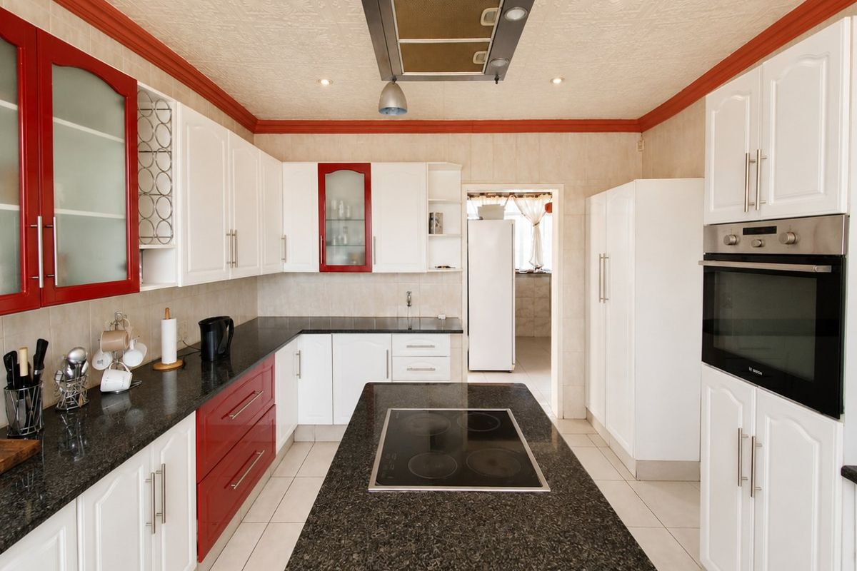 A well-equipped kitchen featuring granite countertops, a central island with an electric hob, built-in oven, and ample cabinetry, leading to a separate scullery area.