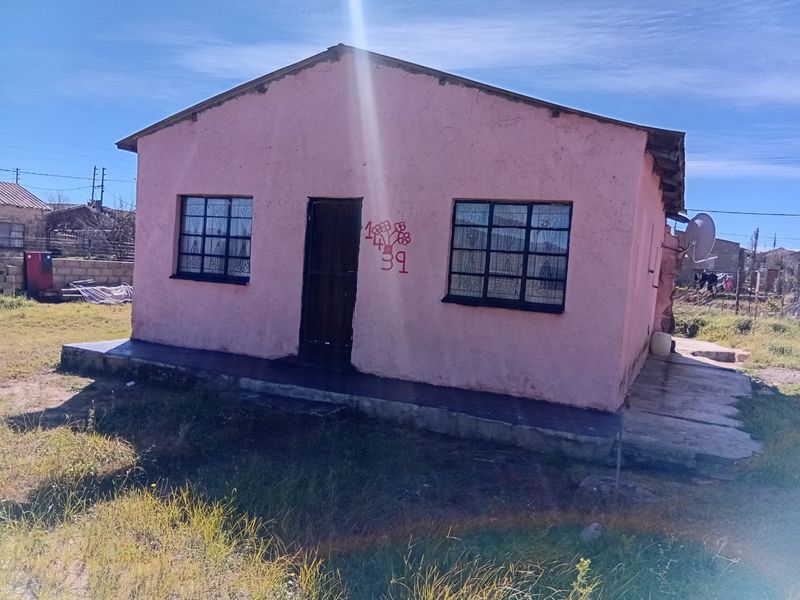 A detached single-story house featuring a pink rendered facade, security bars on windows, and a concrete porch area.