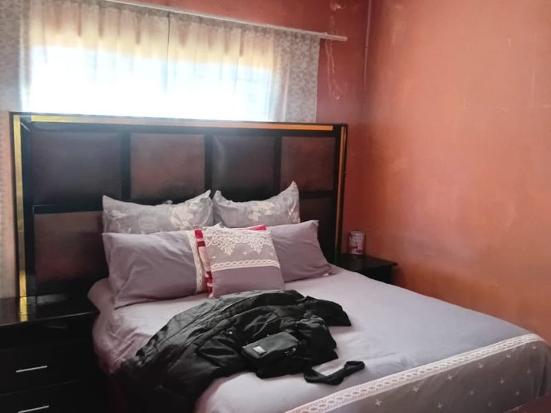A bedroom featuring a built-in headboard, currently showing signs of wear including wall plaster damage and ceiling water staining.