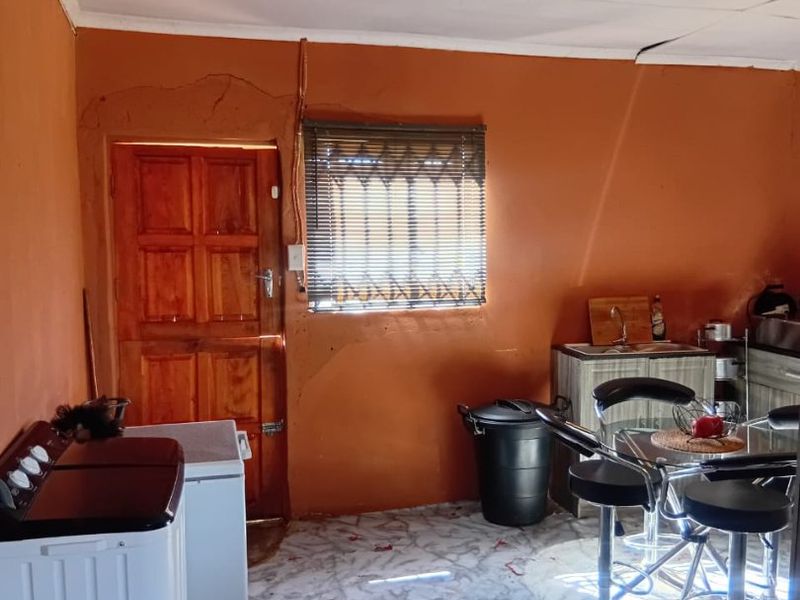 A functional kitchen area featuring tiled flooring, a timber door, and a window with blinds, requiring cosmetic updates to the walls and ceiling.