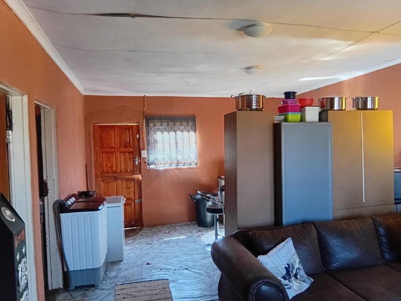Open plan living area featuring terracotta walls, a timber entrance door, and security window bars. The space requires ceiling and wall repairs.