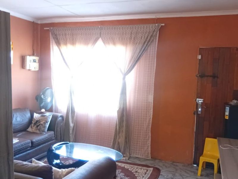 A living room area featuring tiled flooring, a timber door, and an exposed electrical distribution board, requiring cosmetic updates to improve the overall aesthetic.