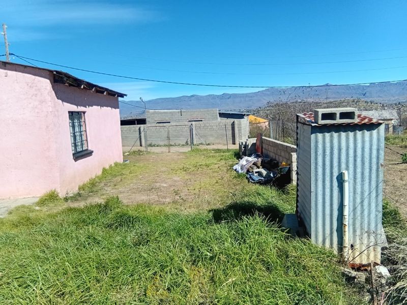 Rear yard area featuring a corrugated iron utility structure, concrete block boundary wall, and views of the surrounding landscape.