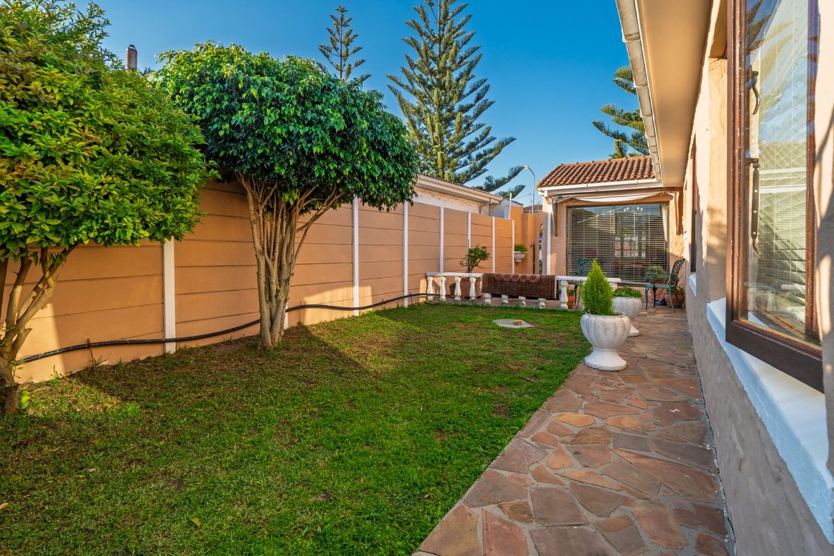 A private rear garden featuring a stone-paved walkway, a well-maintained lawn, and a secure perimeter wall.