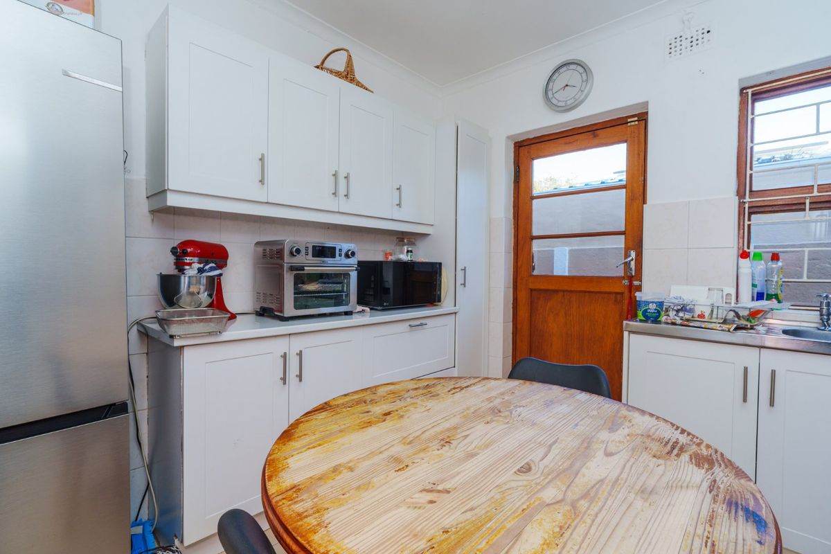 A functional kitchen featuring white cabinetry, tiled splashbacks, and a timber door leading to the exterior.