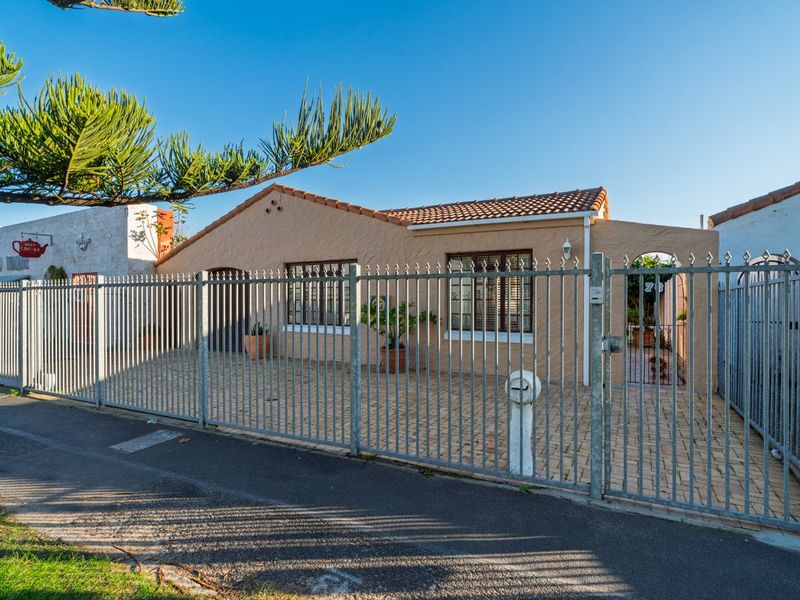 Front view of a single-story house featuring a paved driveway, secure metal fencing, and a classic terracotta tiled roof.