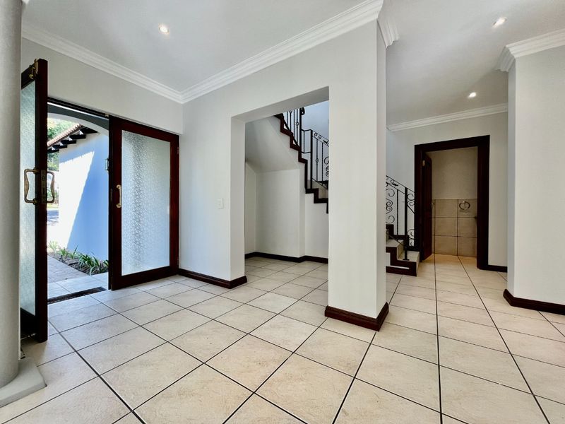 Spacious entrance hall featuring tiled flooring, crown molding, and a staircase with a decorative wrought iron balustrade leading to the upper level.