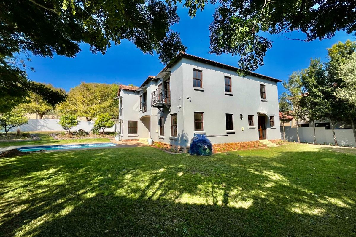 Rear view of a two-story house featuring a swimming pool, manicured lawn, and a small wrought iron balcony.