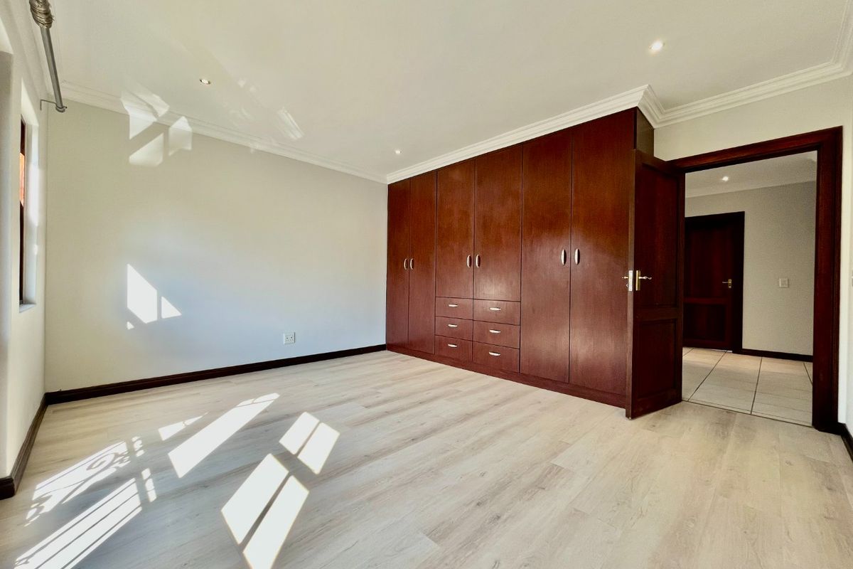 A bright, empty bedroom featuring light-toned laminate flooring, recessed downlighting, and extensive dark wood built-in cabinetry.