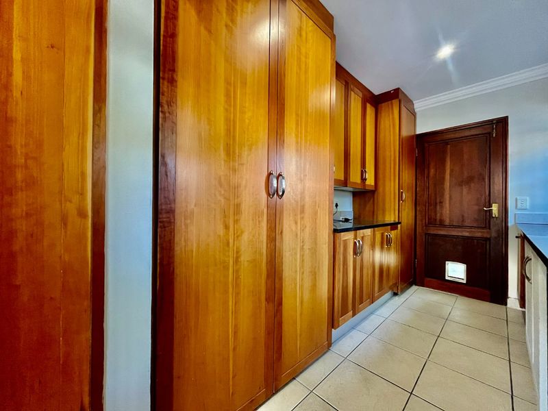 A functional scullery or utility area featuring extensive built-in wooden cabinetry, tiled flooring, and a solid wood door with an integrated pet flap.