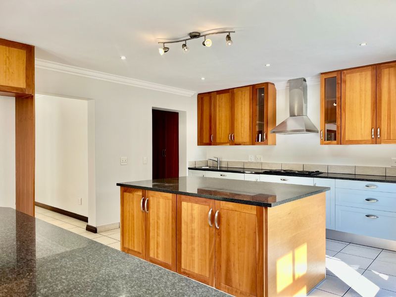 A functional kitchen featuring a central island with granite countertops, wooden cabinetry, stainless steel extractor fan, and tiled flooring.