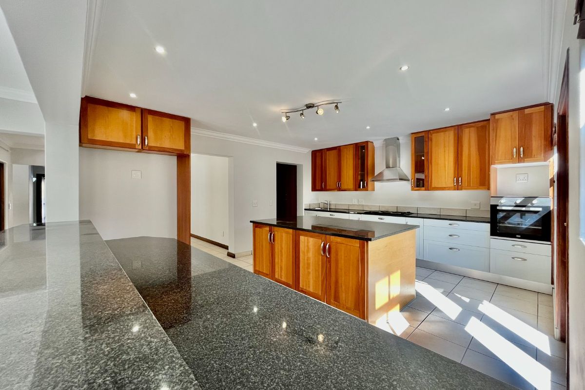 Spacious kitchen featuring a central island, granite countertops, built-in oven, extractor fan, and a mix of wooden and white cabinetry with tiled flooring.