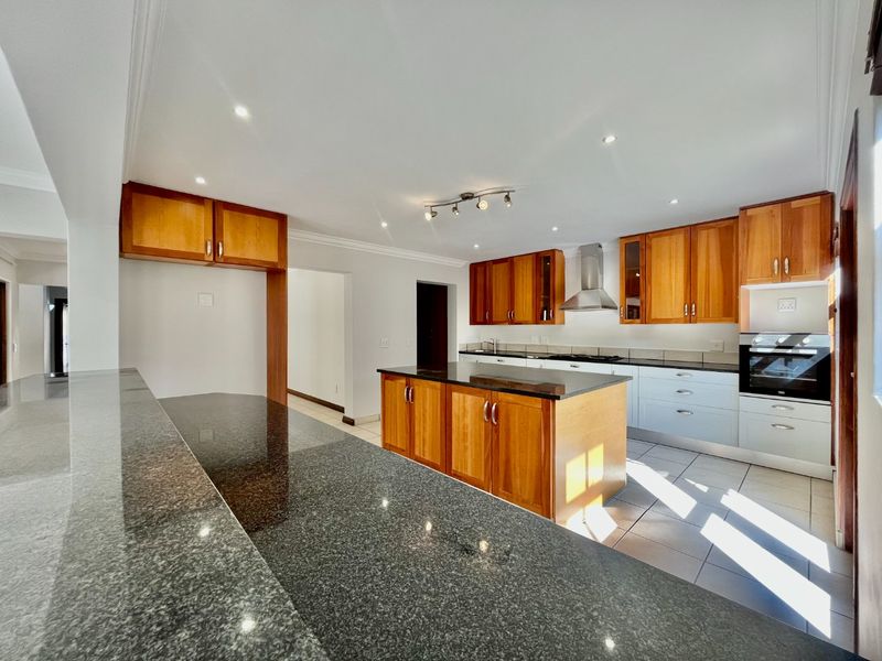 Spacious kitchen featuring a central island, granite countertops, built-in oven, extractor fan, and a mix of wooden and white cabinetry with tiled flooring.