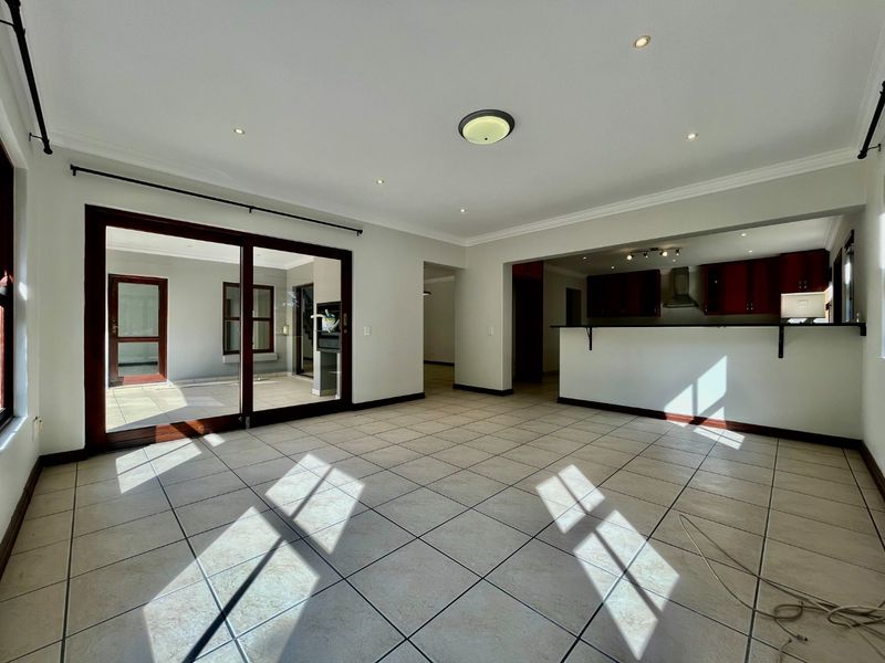 Spacious open-plan living area featuring tiled floors, recessed lighting, and a breakfast bar connecting to the kitchen, with sliding doors leading to the patio.
