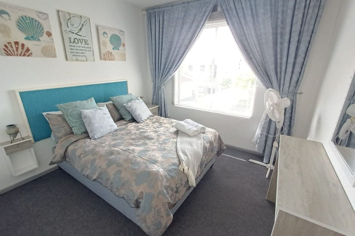 A well-maintained bedroom featuring a built-in headboard, carpeted flooring, and large windows with curtains, providing a comfortable and functional living space.