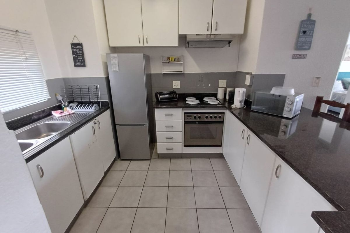 A functional kitchen featuring granite countertops, white cabinetry, built-in oven with hob, extractor fan, and tiled flooring.