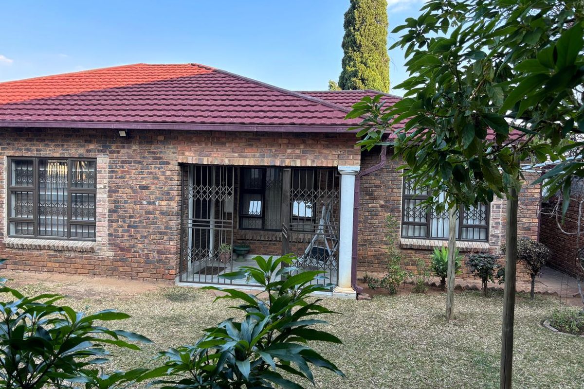 Rear view of a face brick house featuring a covered patio area, tiled roof, and security bars on windows and doors.