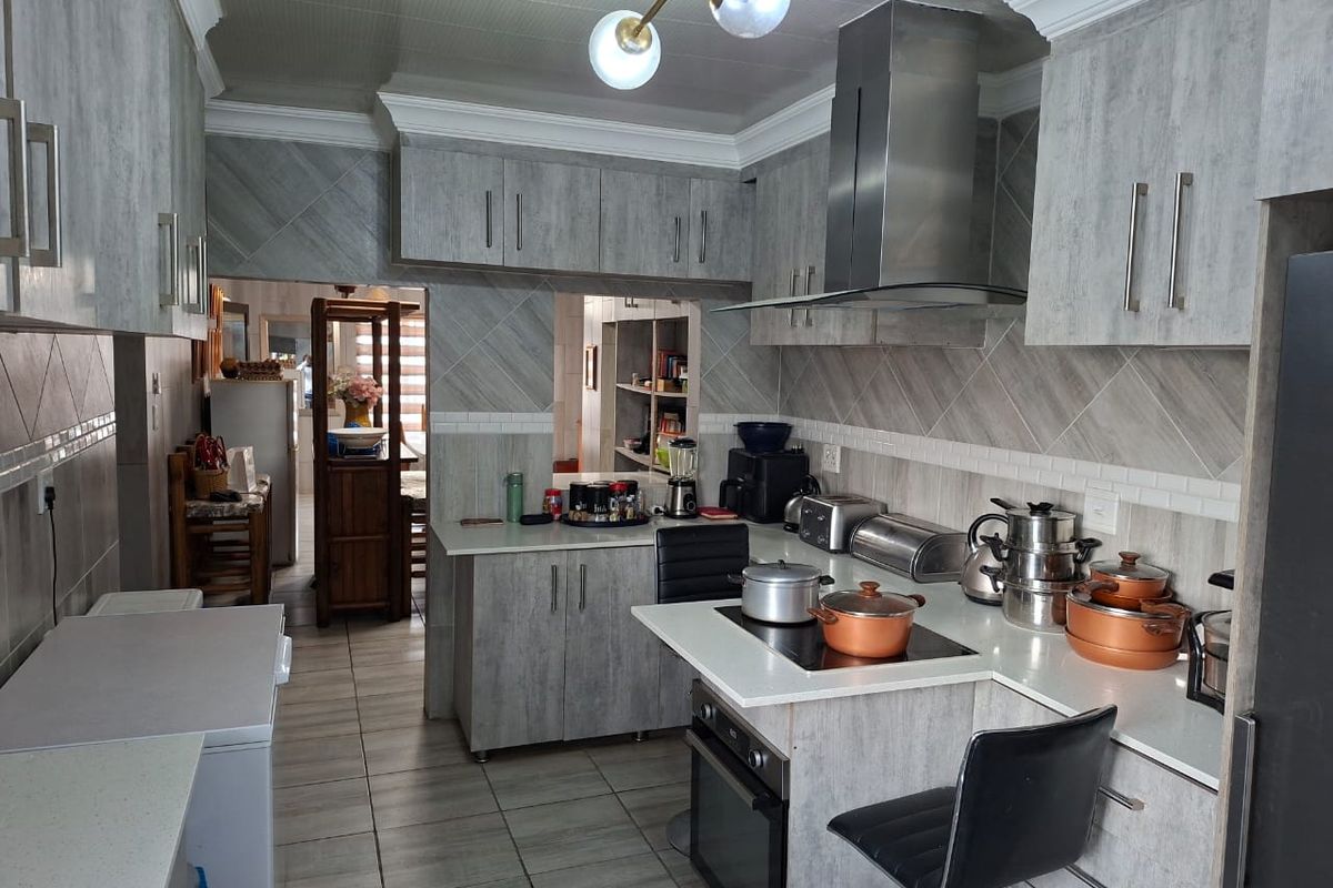 A functional kitchen featuring modern grey cabinetry, a built-in oven and hob, stainless steel extractor fan, and tiled finishes throughout.